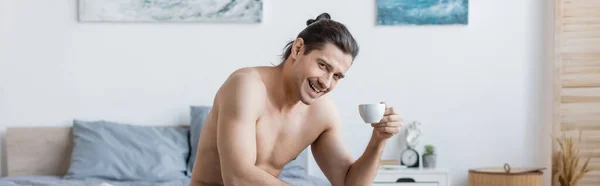 Hombre feliz y sin camisa con el pelo largo sosteniendo la taza de café, bandera - foto de stock