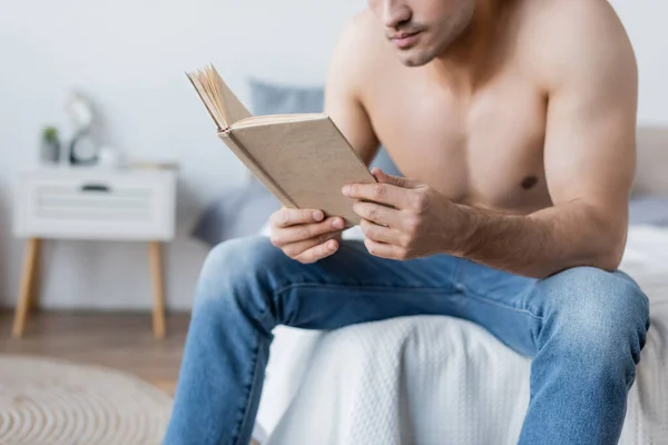 Cropped view of shirtless man reading book while sitting on bed — Stock Photo