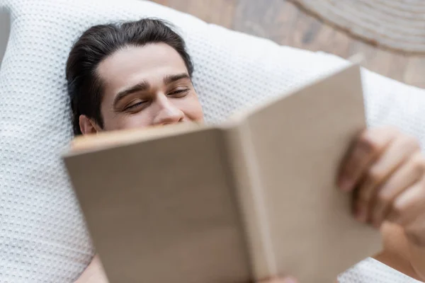 Top view of man covering face while book and lying on bed — Stock Photo