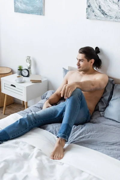 Dreamy barefoot man in jeans resting on bed at home — Stock Photo
