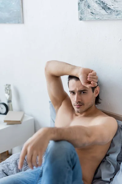 Uomo senza maglietta in jeans guardando la fotocamera mentre riposava sul letto — Foto stock
