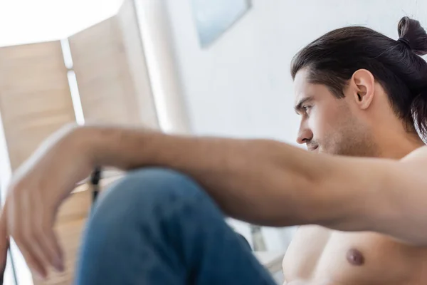 Hombre sin camisa en vaqueros borrosos mirando hacia fuera en casa - foto de stock