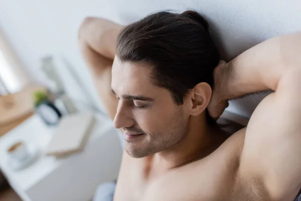 Hombre sin camisa con los ojos cerrados sonriendo mientras descansa en casa - foto de stock