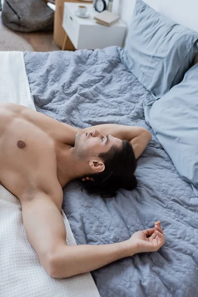 Top view of shirtless man with long hair lying on bed at home — Stock Photo