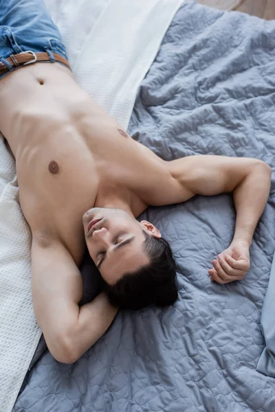 Vue de dessus de l'homme torse nu en jeans couché sur le lit — Photo de stock