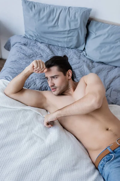 Vista ad alto angolo di uomo senza camicia sdraiato sul letto — Foto stock