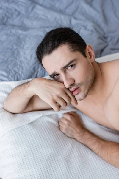 Hochwinkelaufnahme eines hemdlosen Mannes, der auf dem Bett liegt und in die Kamera schaut — Stockfoto