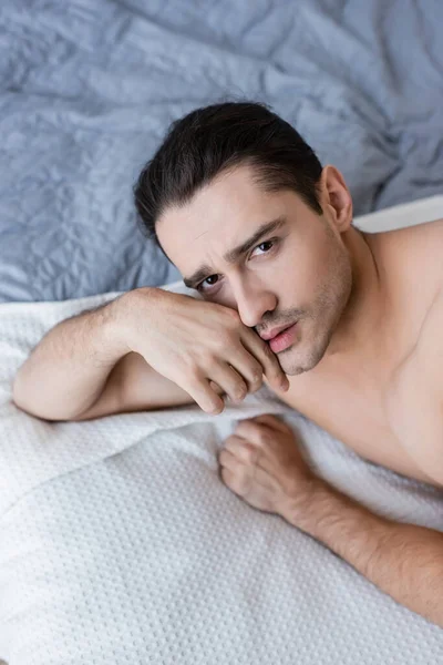 Vista de ángulo alto del hombre sin camisa acostado en la cama y mirando a la cámara - foto de stock