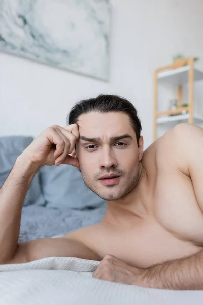 Hemdloser Mann ruht sich auf Bett aus und blickt in Kamera — Stockfoto