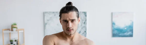 Hombre sin camisa con el pelo largo mirando a la cámara en casa, pancarta - foto de stock