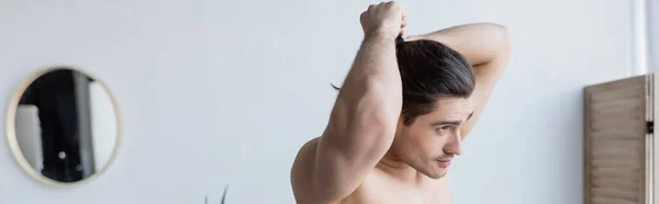 Homme musclé ajuster les cheveux longs tout en se tenant debout dans la salle de bain moderne, bannière — Photo de stock