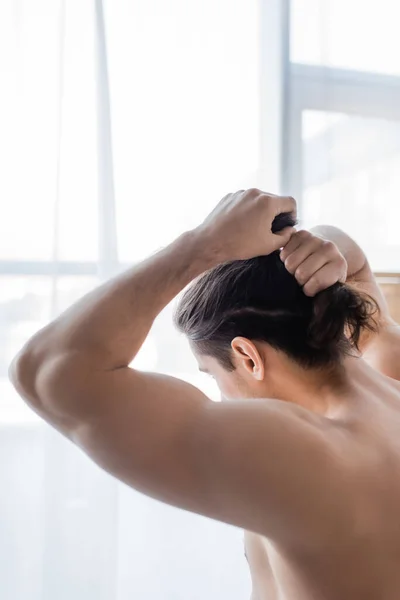 Vista posterior del hombre musculoso ajustando el pelo largo en el baño - foto de stock