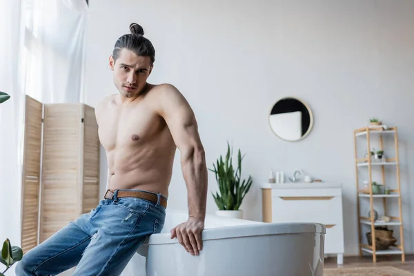 Hemdloser Mann mit langen Haaren sitzt in Badewanne im modernen Badezimmer — Stockfoto