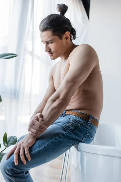 Shirtless man with long hair sitting on white bathtub — Stock Photo