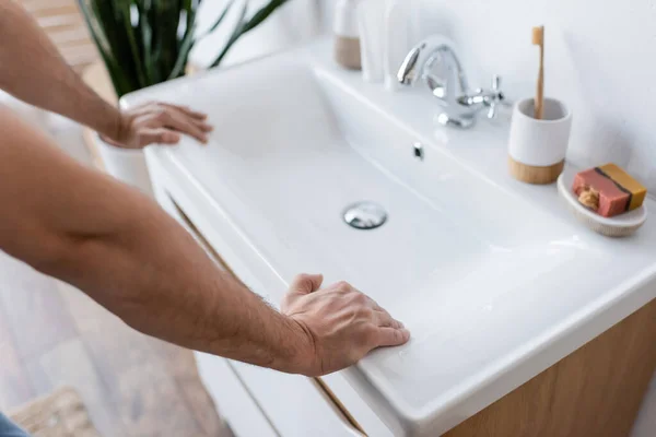 Обрезанный вид человека, опирающегося на белую раковину в ванной комнате — стоковое фото