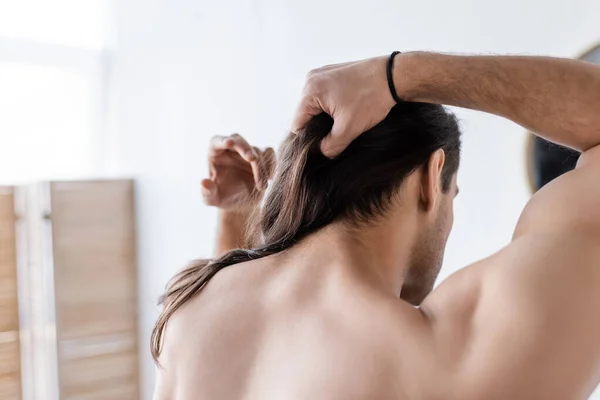 Rückseite des hemdlosen Mannes, der lange Haare im Badezimmer stylt — Stockfoto