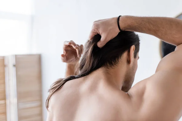 Vista trasera del hombre sin camisa peinado pelo largo en el baño - foto de stock