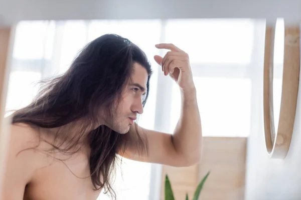 Vue latérale de l'homme torse nu coiffant les cheveux longs près du miroir — Photo de stock