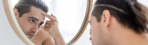 Man applying face cream and looking at mirror, banner — Stock Photo