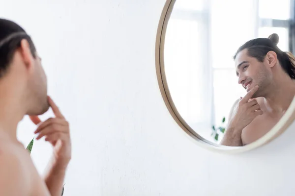 Hombre alegre y sin camisa sonriendo mientras mira el espejo en el baño - foto de stock