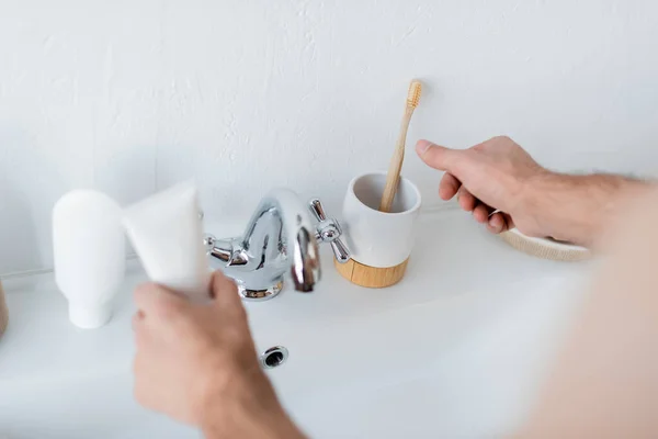 Vista recortada del hombre sosteniendo el tubo de pasta de dientes en el baño - foto de stock