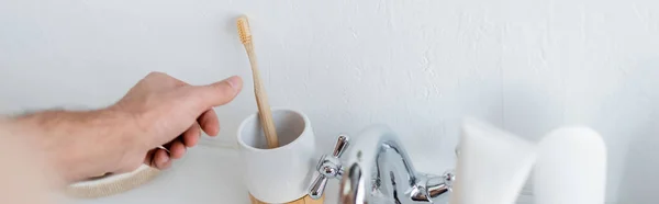 Cropped view of man holding reaching toothbrush in bathroom, banner — Stock Photo