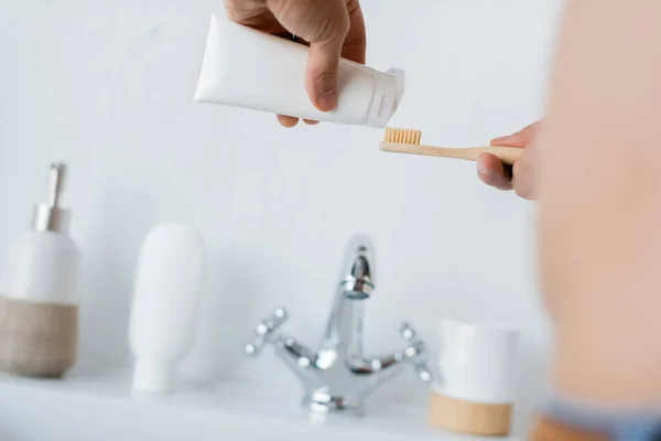 Vista recortada del hombre apretando la pasta de dientes en el cepillo de dientes en el baño - foto de stock