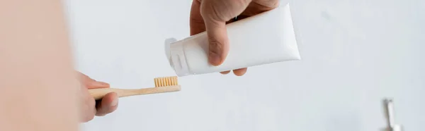 Vista recortada del hombre apretando la pasta de dientes en el cepillo de dientes en el baño, pancarta - foto de stock
