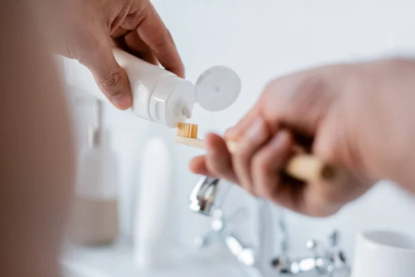 Partial view of man squeezing toothpaste on toothbrush in bathroom — Stock Photo