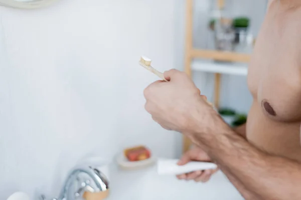 Vista parziale dell'uomo che tiene lo spazzolino da denti con dentifricio in bagno — Foto stock