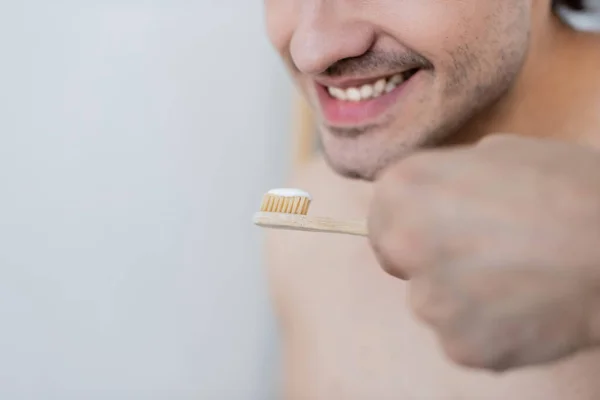Vista recortada de hombre alegre sosteniendo cepillo de dientes con pasta de dientes en el baño - foto de stock