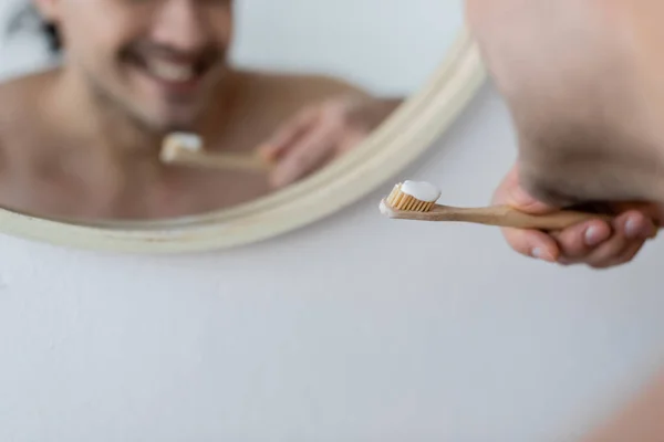 Hombre cortado y alegre sosteniendo cepillo de dientes con pasta de dientes en el baño - foto de stock