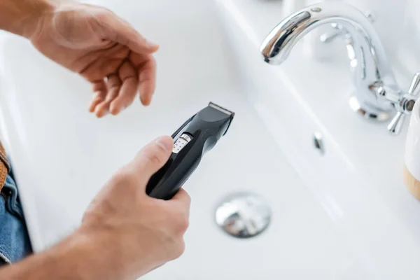 Vista recortada del hombre sosteniendo maquinilla de afeitar eléctrica en el baño - foto de stock