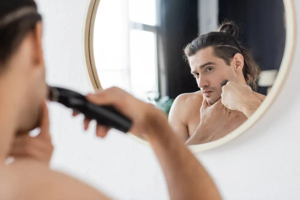 Homem de barbear com lâmina elétrica perto do espelho no banheiro — Fotografia de Stock