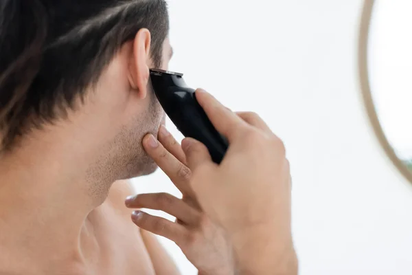 Homme garniture avec rasoir électrique près du miroir dans la salle de bain — Photo de stock