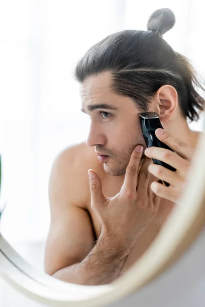 Hombre guapo afeitándose con afeitadora eléctrica en el baño - foto de stock