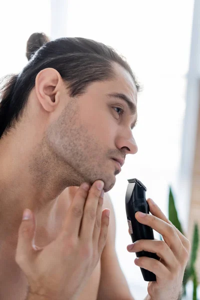 Hombre guapo afeitándose con afeitadora eléctrica en el baño - foto de stock