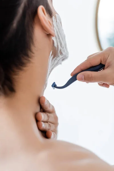 Blurred man with foam on face shaving in bathroom — Stock Photo