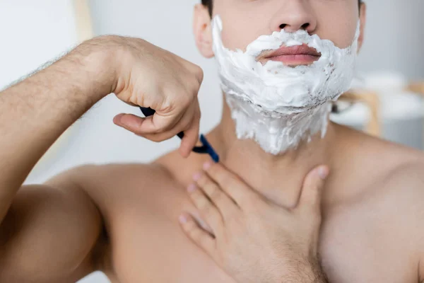 Partial view of shirtless man with foam on face shaving in bathroom — Stock Photo