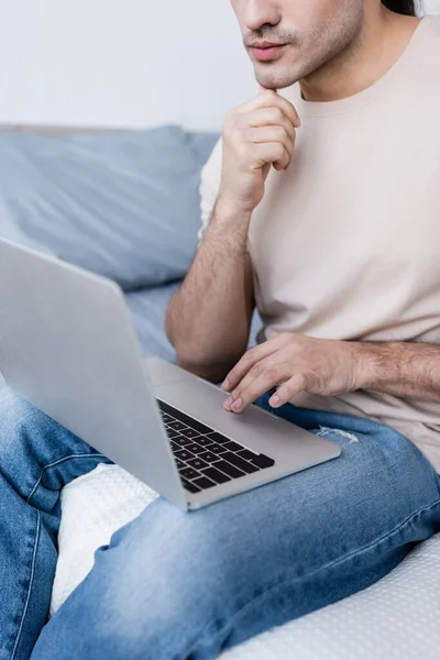 Vista recortada del freelancer sentado en la cama y utilizando el ordenador portátil - foto de stock