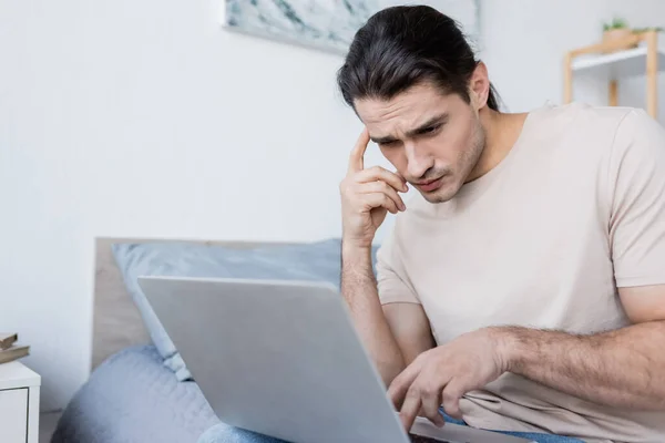 Freelancer pensativo usando el ordenador portátil en el dormitorio - foto de stock