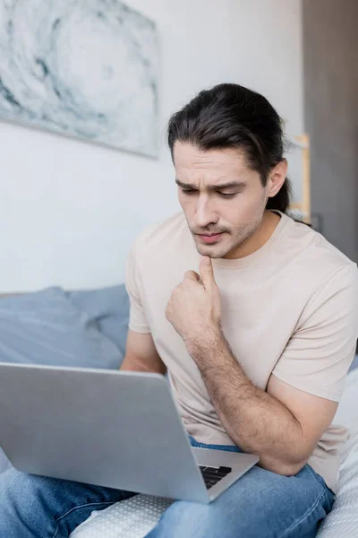 Pensativo freelancer utilizando el ordenador portátil en el dormitorio - foto de stock