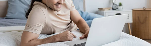 Cropped view of cheerful freelancer using laptop in bedroom, banner — Stock Photo