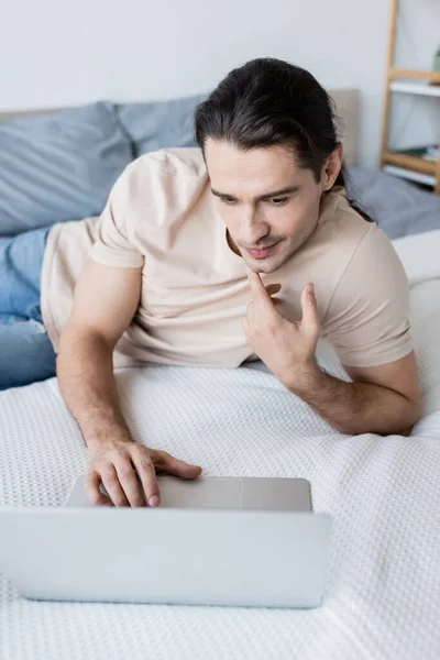 Nachdenklicher Mann blickt auf Laptop im Schlafzimmer — Stockfoto