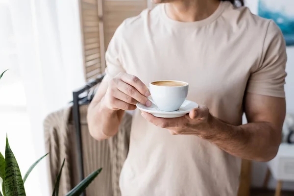 Vista ritagliata dell'uomo in t-shirt con piattino con tazza di caffè — Foto stock