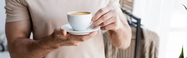 Cropped view of man in t-shirt holding saucer with cup of coffee, banner — Stock Photo