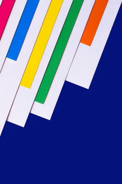 Multicolored diagonal paper stripes on blue background with copy space — Stock Photo