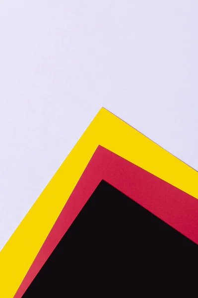 Hojas de papel negro, rojo y amarillo sobre fondo lavanda claro - foto de stock