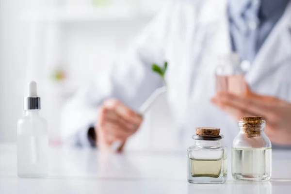 Bottles with essential oils near serum and blurred chemist in lab — Stock Photo