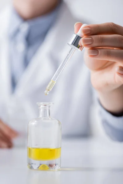 Cropped view of laboratory assistant holding pipette near bottle with serum — Stock Photo